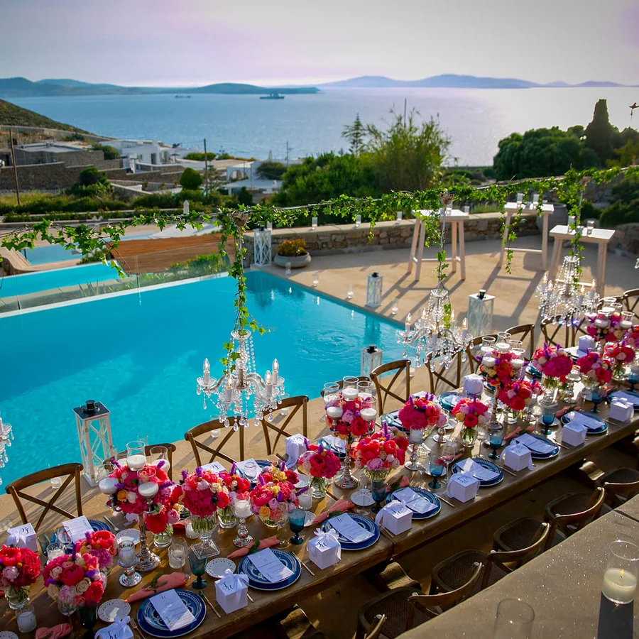Long table dressed with flowers and chandeliers beside a pool above the sea in Mykonos