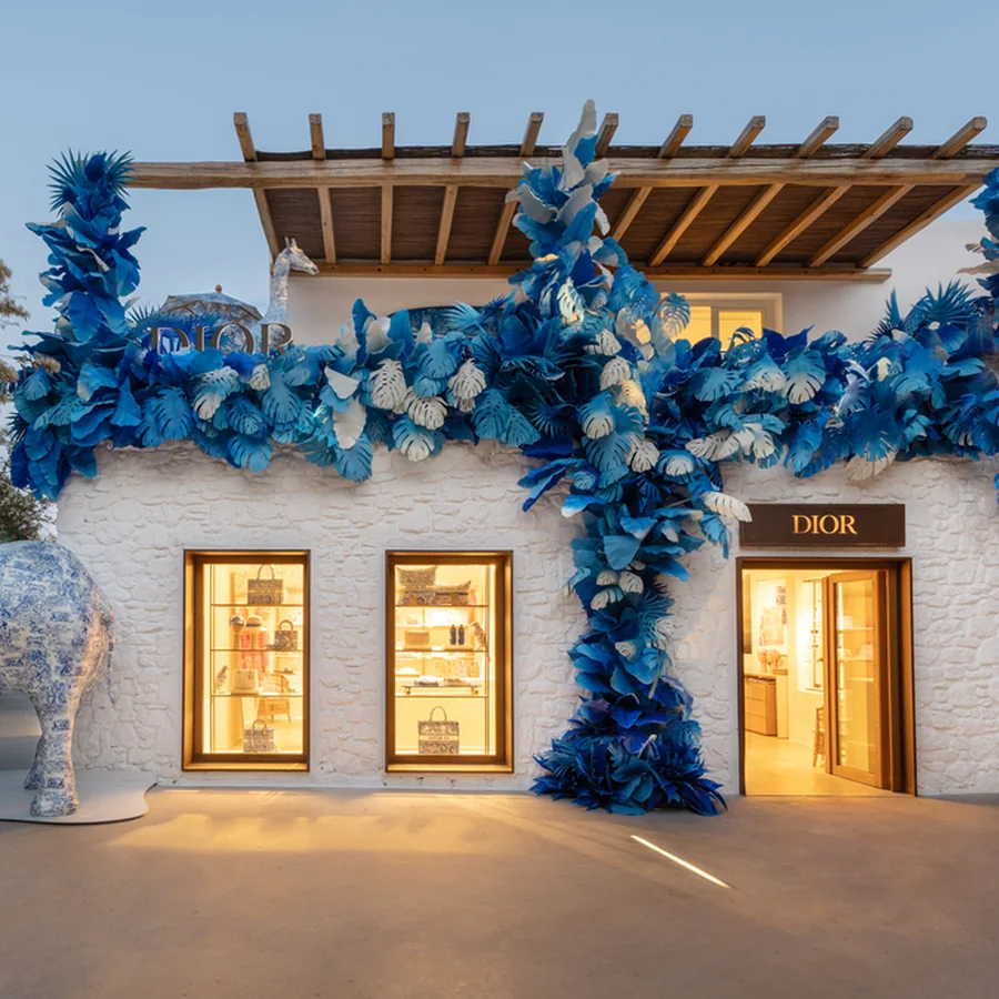 Designer boutique in Mykonos decorated with blue leaves, its windows lit at dusk