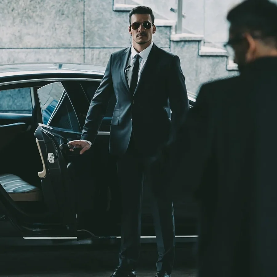 Security officer in a dark suit holding a car door open