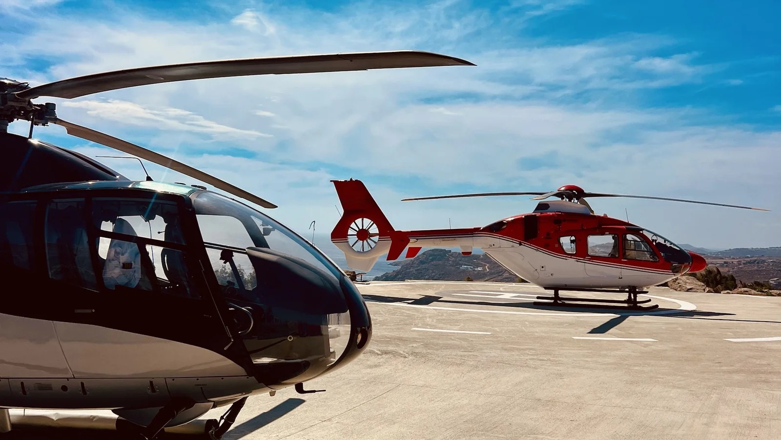 Two private helicopters on a helipad above the Mykonos coast
