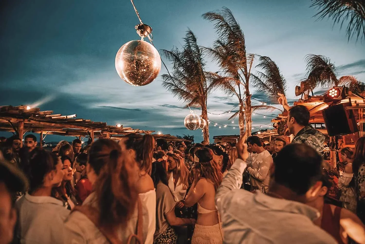 Disco balls above a crowd dancing at a Mykonos beach party at dusk