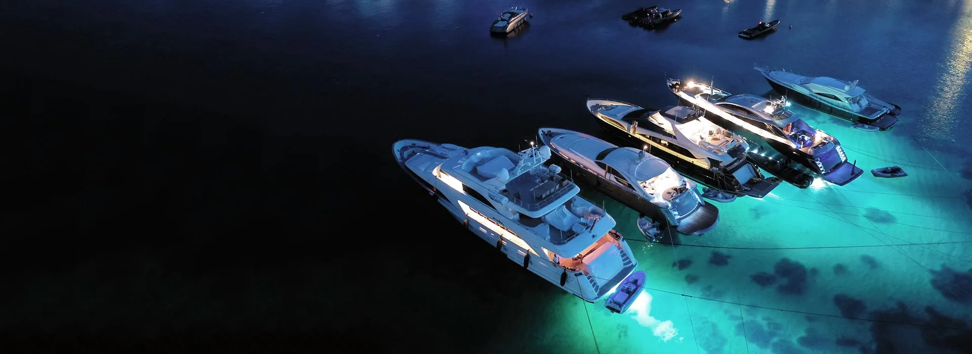 Yachts at anchor at night, their lights turning the water turquoise